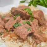Slow Cooker Beef Tips and Gravy features tender chunks of cooked beef garnished with chopped parsley, served over a bed of rice and topped with rich brown sauce.