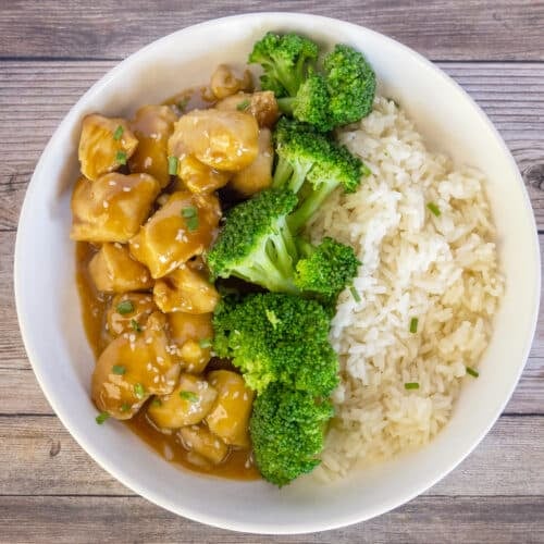 A white bowl with white rice, steamed broccoli, and chicken pieces in a brown sauce, viewed from above on a wooden surface—one of those easy dinners that quickly becomes a family favorite.