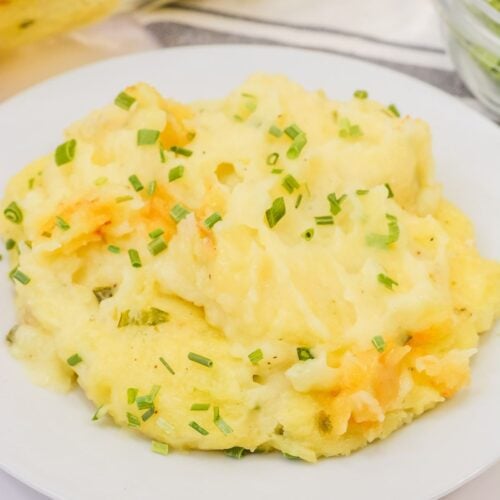 A serving of cheesy Baked Twice Mashed Potatoes topped with chopped chives is presented on a white plate for a comforting, savory dish.