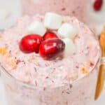 A glass filled with a pink creamy Cranberry Fluff salad mixture, topped with three cranberries and three mini marshmallows—an irresistible holiday dessert.
