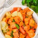 Bowl of the root vegetables with onions, garnished with parsley, served alongside a fork and fresh parsley.