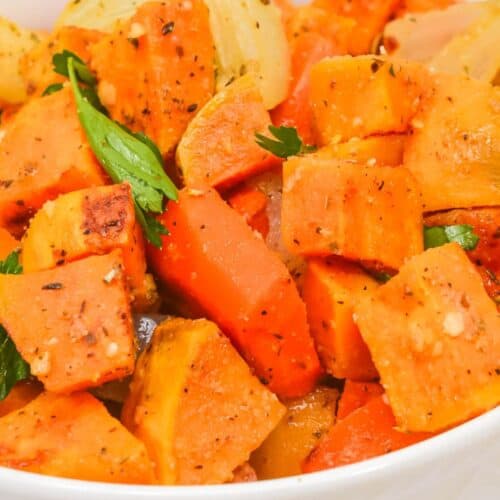 A bowl of Roasted Sweet Potatoes and Carrots, mixed with onions and garnished with fresh herbs, makes a colorful and flavorful side dish.