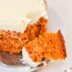 A slice of Vintage Tomato Soup Cake with cream cheese frosting sits on a white plate, a fork holding a bite-sized piece.