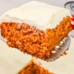 A close-up of a slice of Vintage Tomato Soup Cake with cream cheese frosting being lifted from a baking dish.