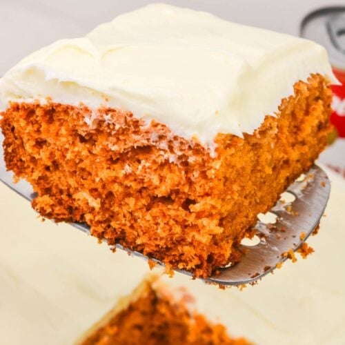 A close-up of a slice of Vintage Tomato Soup Cake with cream cheese frosting being lifted from a baking dish.