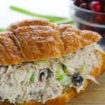 A croissant sandwich featuring celery and dried cranberries—sits in front of a bowl brimming with fresh cranberries.