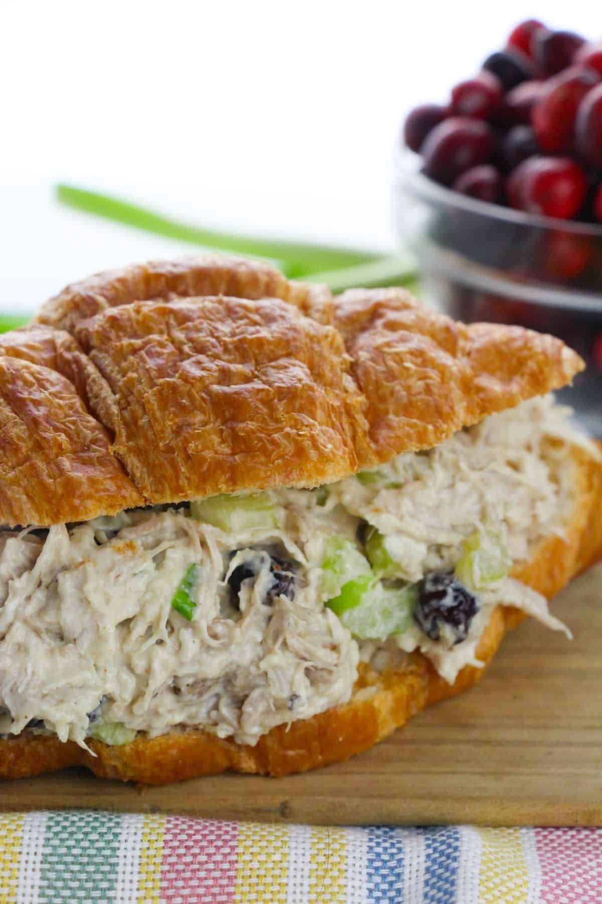 A croissant sandwich featuring celery and dried cranberries—sits in front of a bowl brimming with fresh cranberries.