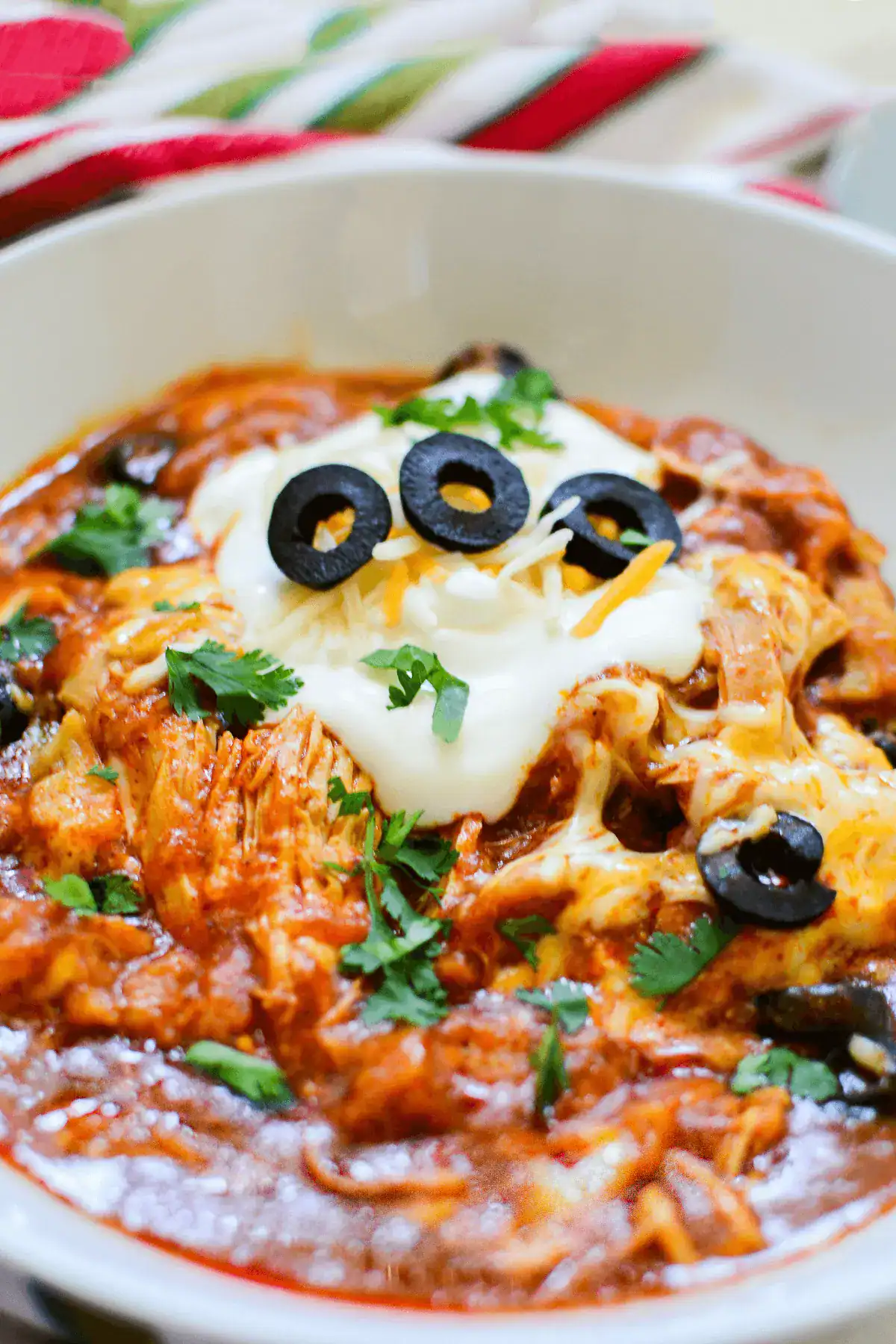 A bowl of shredded chicken enchiladas topped with melted cheese, sour cream, sliced black olives, and chopped cilantro—perfect for those looking for easy slow cooker recipes or convenient self-cooking meals.