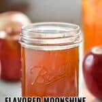 A mason jar filled with orange-colored moonshine sits on a table, surrounded by apples and cinnamon sticks. Text reads: "Flavored moonshine recipes that pack a punch—discover bold and unique twists on classic moonshine recipes.