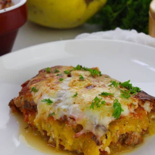 A slice of Spaghetti Squash Lasagna casserole, topped with melted cheese and chopped parsley, served on a white plate.