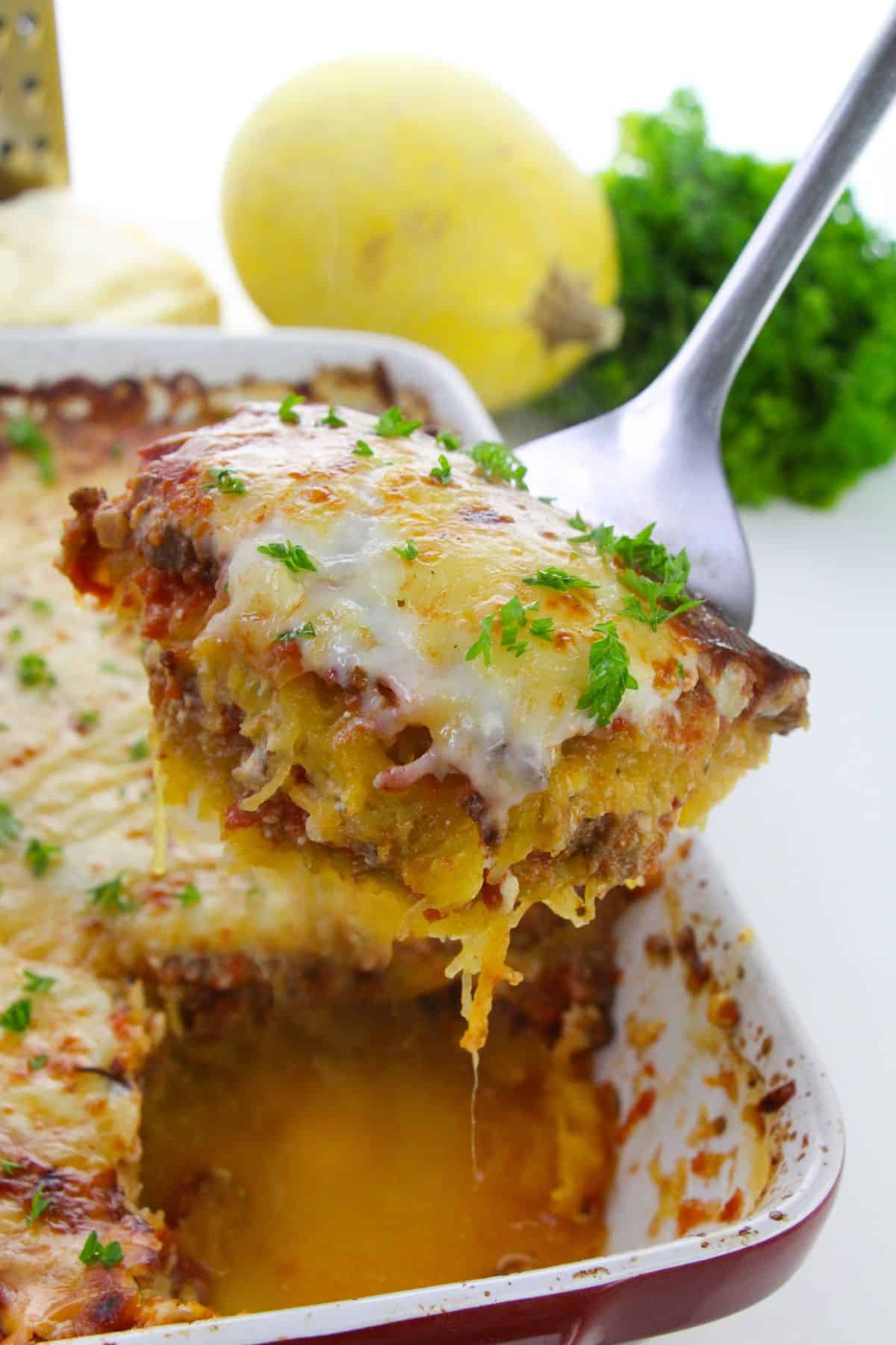 A slice  with savory meat and herbs is being lifted from a baking dish.