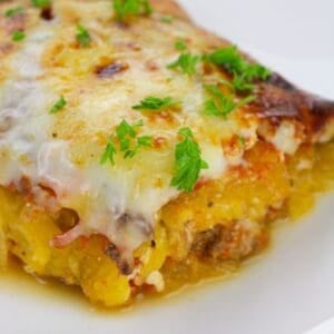 Close-up of a slice of Spaghetti Squash Lasagna topped with melted cheese and garnished with fresh parsley on a white plate.