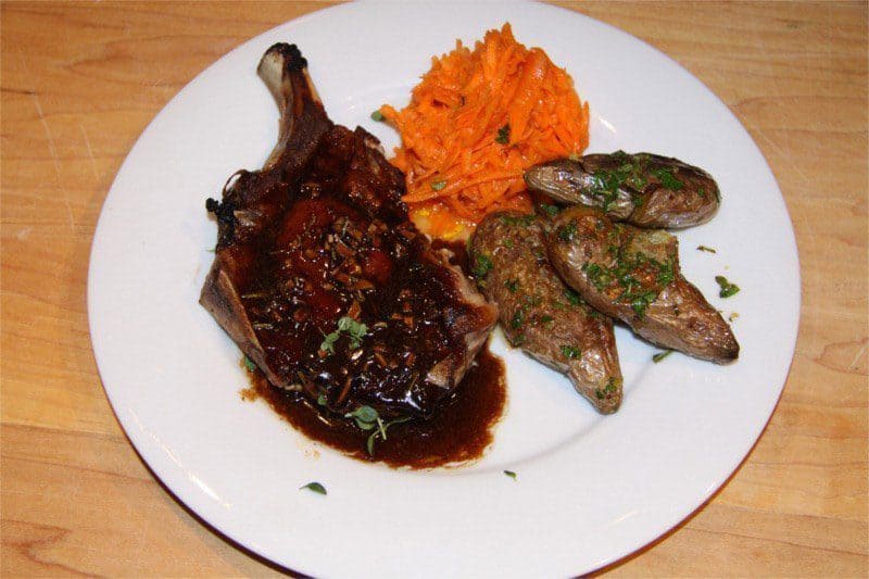 Enjoy these delicious pork chops with dark sauce, accompanied by seasoned fingerling potatoes and a serving of shredded carrot salad on a white plate—a simple yet elegant addition to your collection of easy pork chop recipes.