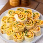 A plate with cheese, bacon, and greens is arranged in a circular pattern on a white plate. Salt and pepper shakers are in the background.