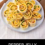 A white plate holds neatly arranged Pepper Jelly Pinwheels—tortilla appetizers filled with pepper jelly, cheese, and greens. The text reads "Pepper Jelly Pinwheels.