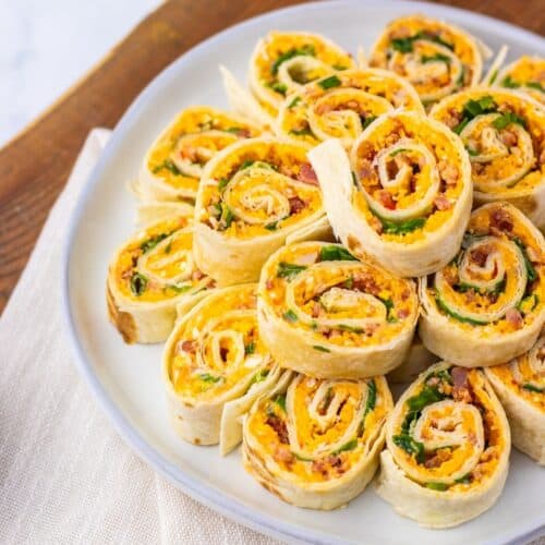 A plate of sliced Pepper Jelly Pinwheels filled with cheese, vegetables, and deli meat, arranged in a layered spiral pattern on a white plate.