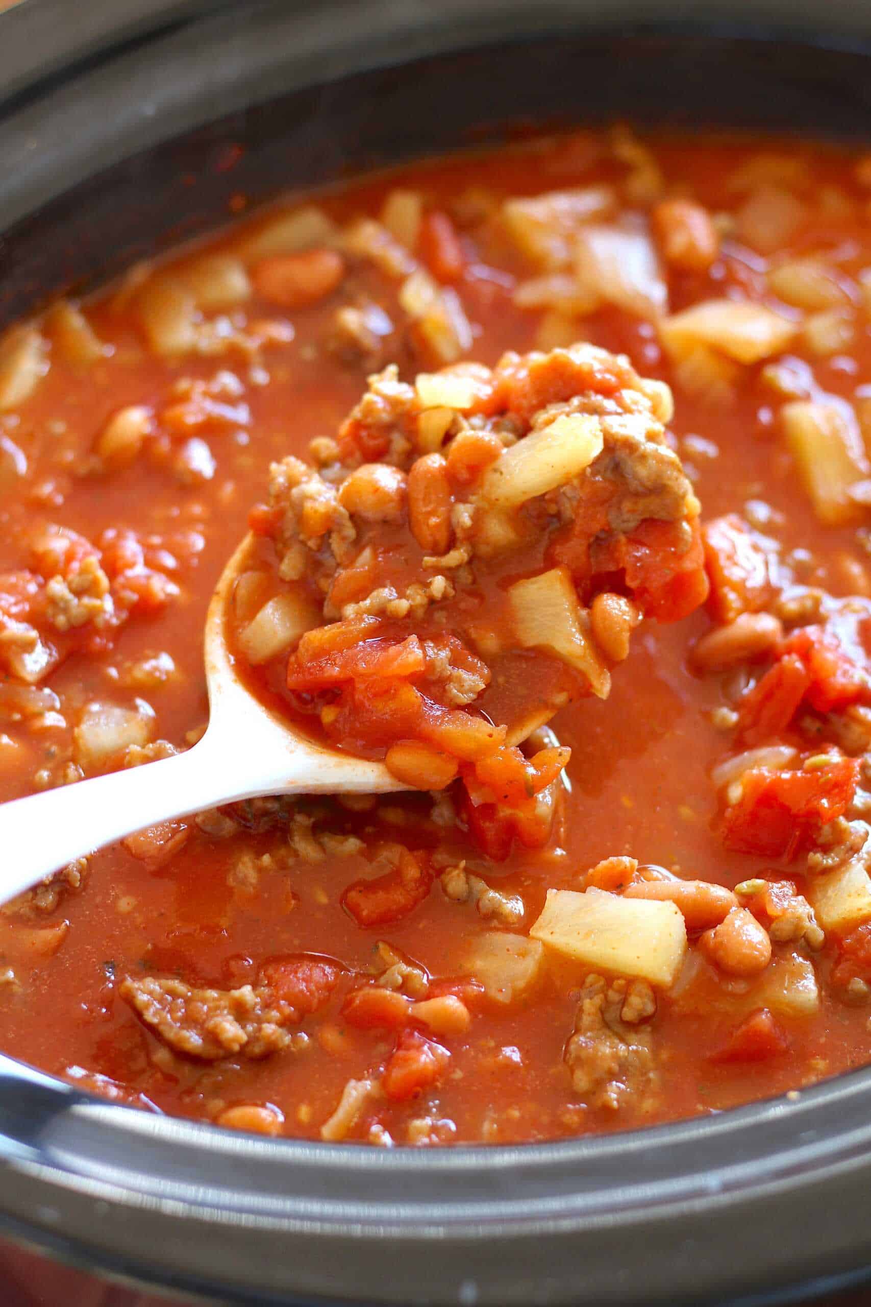 A ladle lifts a serving of hearty chili with beans, ground beef, tomatoes, and onions from a pot—one of those must try chili recipes that always hits the spot.