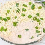 A glass dish filled with Salsa and Cream Cheese Dip, topped with shredded cheese and chopped green onions, with a bunch of fresh green onions beside it.
