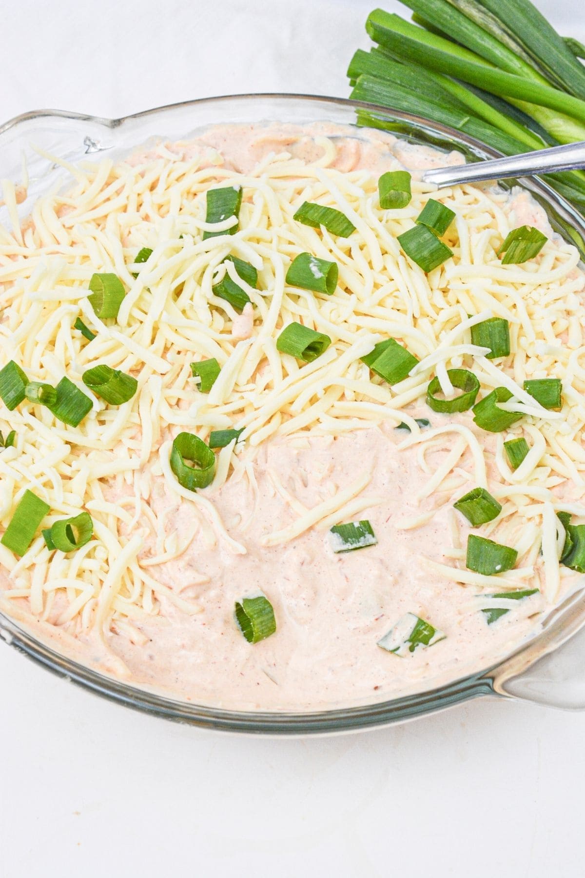 A glass dish topped with shredded cheese and chopped green onions, with a bunch of fresh green onions beside it.