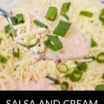 A spoonful of Salsa and Cream Cheese Dip, topped with shredded cheese and chopped green onions, held above a bowl brimming with the same irresistible dip.