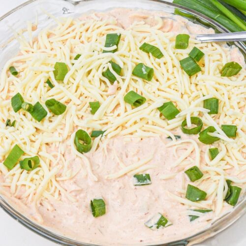 A glass dish filled with Salsa and Cream Cheese Dip, topped with shredded cheese and chopped green onions, with whole green onions placed beside the dish.