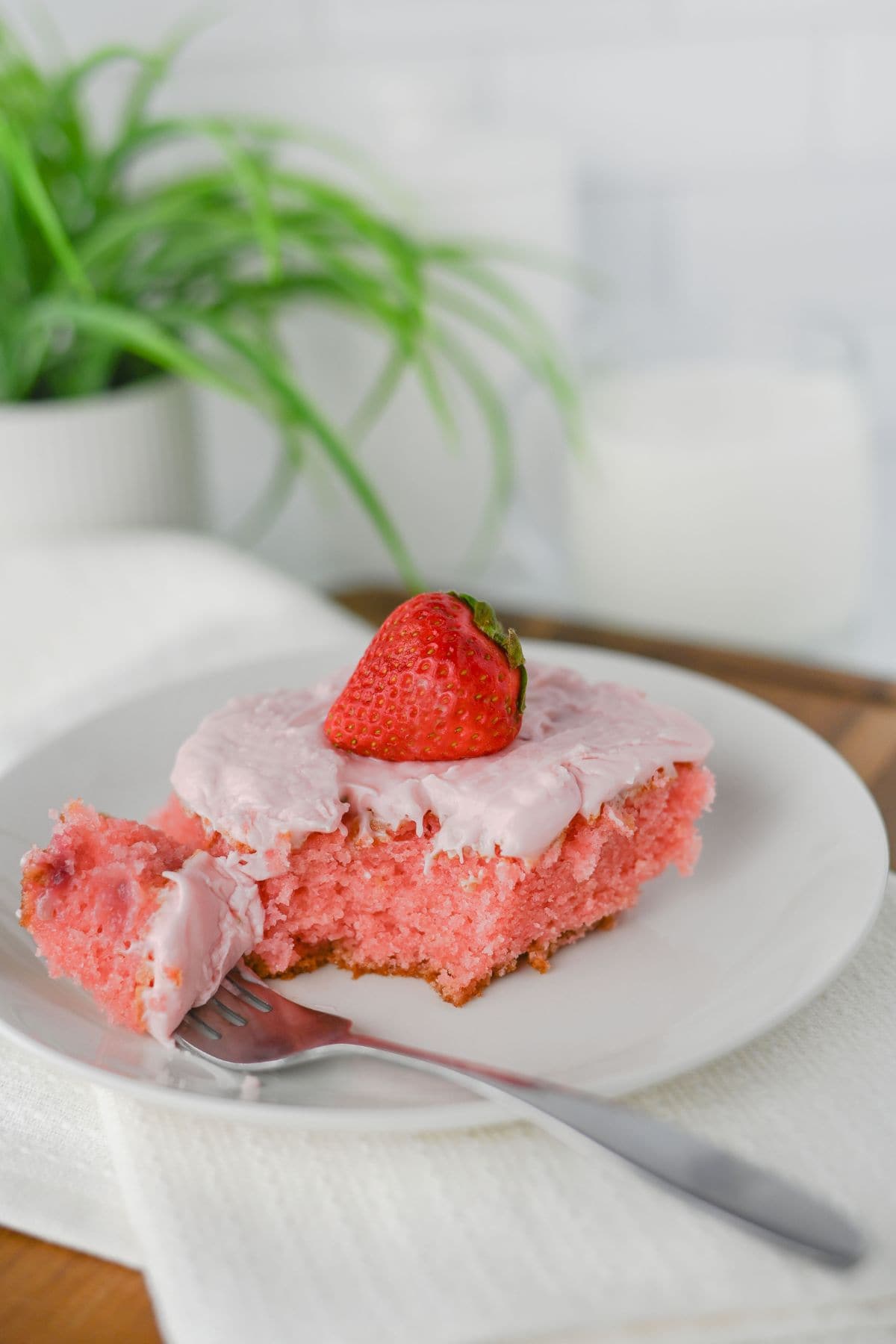 A slice with pink frosting and a whole piece of fruit on top, served on a white plate with a fork.