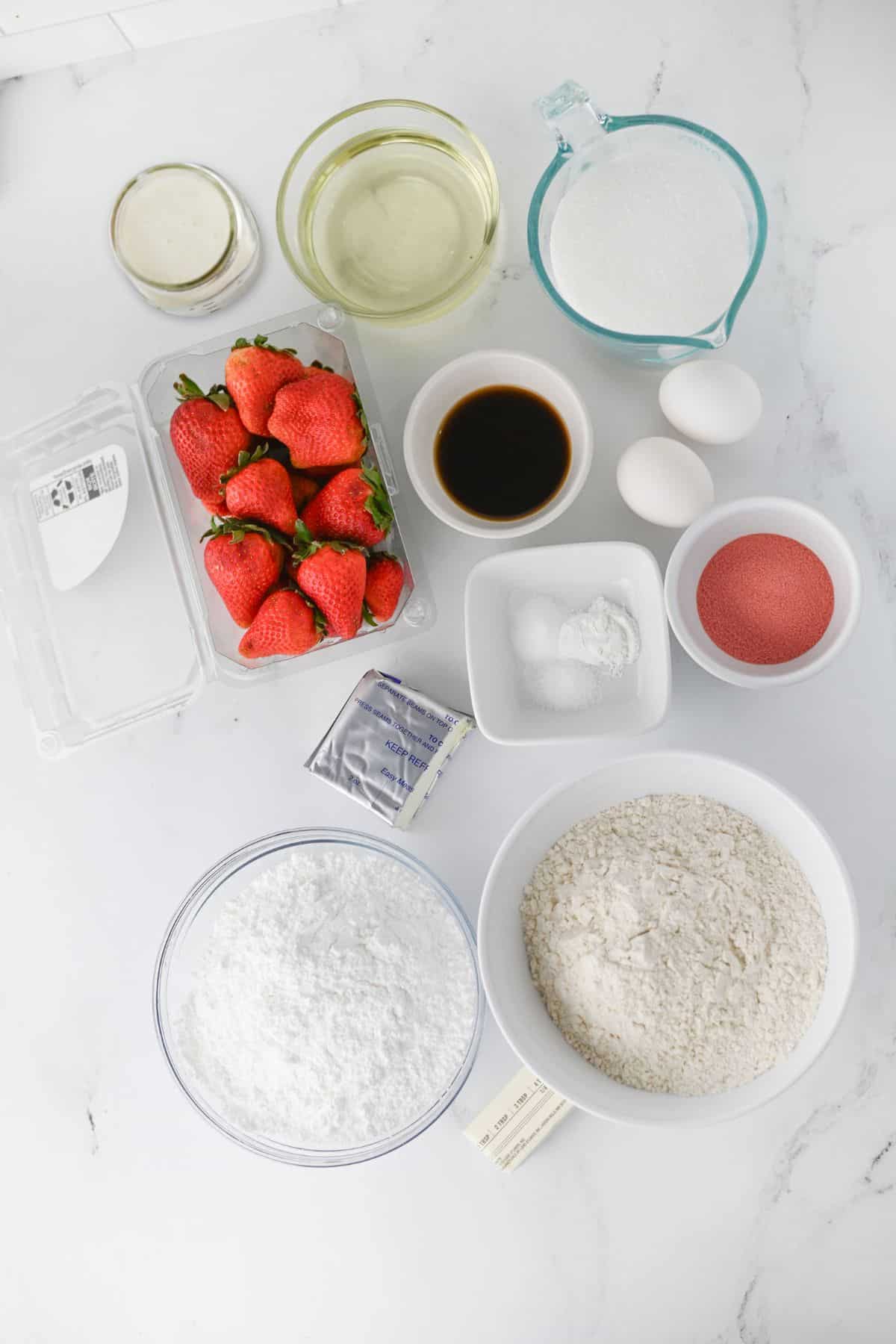 Various baking ingredients for a Homemade Strawberry Cake, including fresh strawberries, sugar, flour, eggs, vanilla extract, oil, baking powder, baking soda, and powdered sugar, are arranged on a white surface.