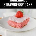 A slice of Homemade Strawberry Cake with pink frosting and a whole strawberry on top, served on a white plate.