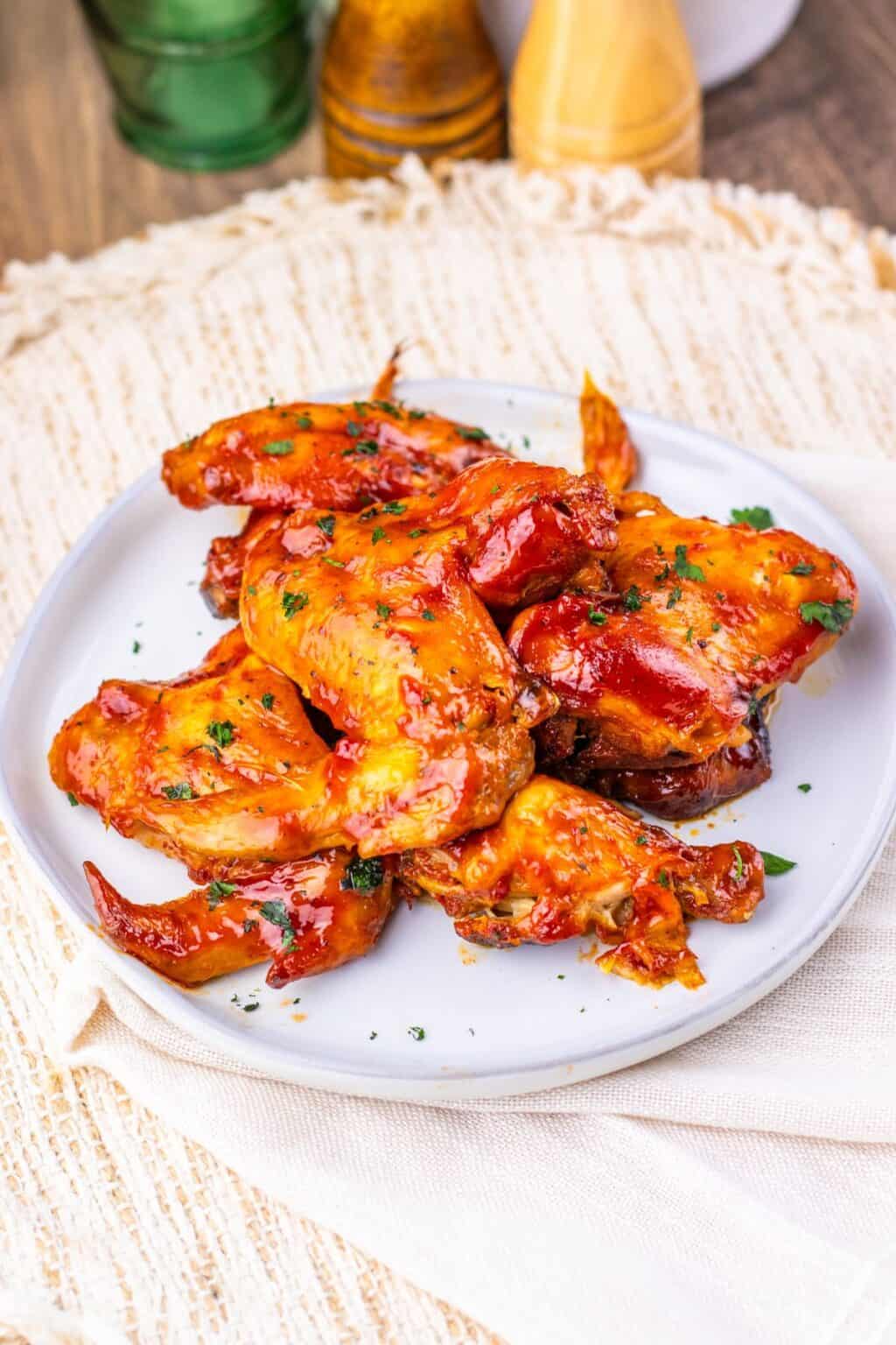 A white plate with several glazed Slow Cooker Chicken Wings garnished with herbs, placed on a light-colored woven placemat.