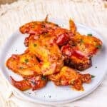 A white plate with several glazed Slow Cooker Chicken Wings garnished with herbs, placed on a light-colored woven placemat.