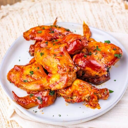 A white plate with several glazed Slow Cooker Chicken Wings garnished with herbs, placed on a light-colored woven placemat.