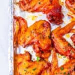 Slow Cooker Chicken Wings baked and coated in a zesty red sauce are arranged on a foil-lined baking sheet, then garnished with fresh chopped herbs.