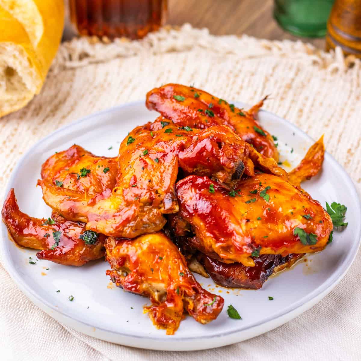 A white plate with several pieces of glazed Slow Cooker Chicken Wings garnished with chopped parsley on a woven placemat.