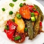A white plate with white rice and Sheet Pan Chicken with Vegetables—stir-fried chicken, red bell peppers, snap peas, and green onions—garnished with sesame seeds.