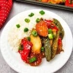 A plate of white rice with carrots, bell peppers, and snap peas, garnished with green onions and sesame seeds.