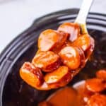 A spoonful in a thick, reddish-brown sauce held over a black crockpot.