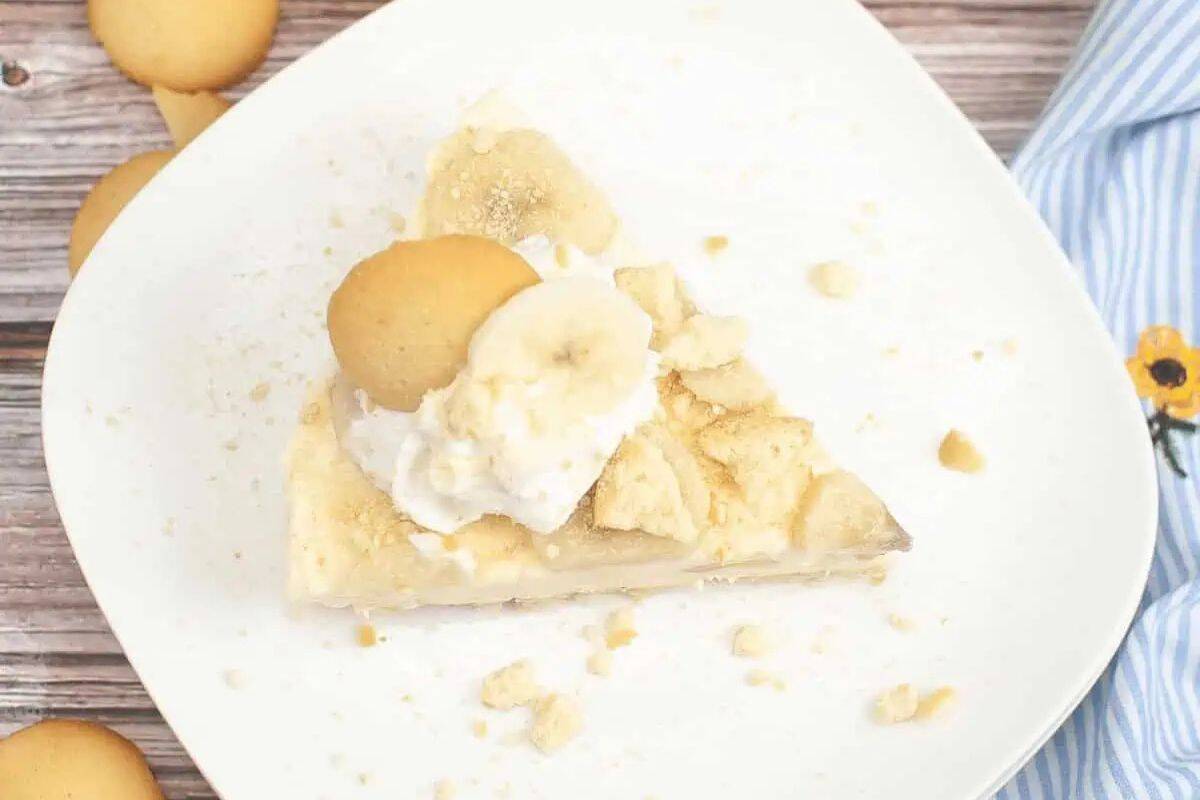 A slice of banana pudding pie topped with whipped cream, banana slices, and crumbled vanilla wafers on a white plate—one of the prettiest desserts to brighten up your table and perfect for spring recipes.