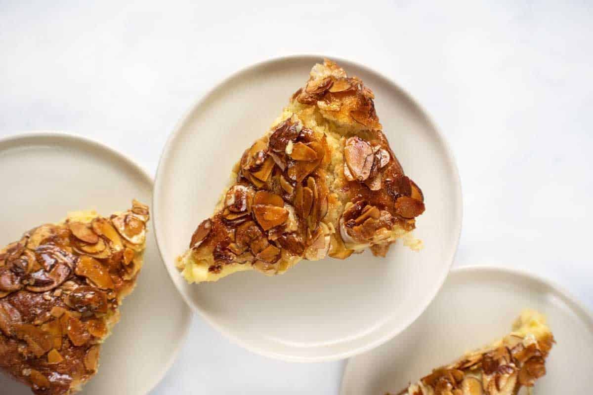 Three of the prettiest desserts—slices topped with glazed almond flakes—are served on small white plates against a light background.