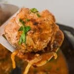 A cooked Hamburger Steak with Onion Gravy is lifted on a metal spatula, garnished with chopped parsley.
