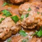 Close-up of Hamburger Steak with Onion Gravy, featuring Salisbury steak patties in brown gravy, garnished with chopped parsley and sliced onions.