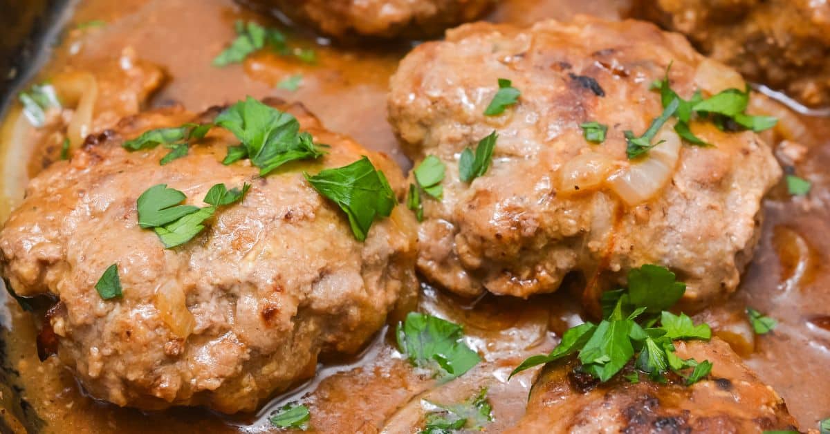 Close-up of Hamburger Steak with Onion Gravy, featuring Salisbury steak patties in brown gravy, garnished with chopped parsley and sliced onions.