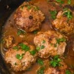 Five browned meat patties simmer in a skillet garnished with chopped parsley.