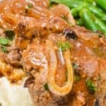 Salisbury steak with onion gravy, also known as Hamburger Steak with Onion Gravy, served over mashed potatoes and accompanied by green beans on a white plate.