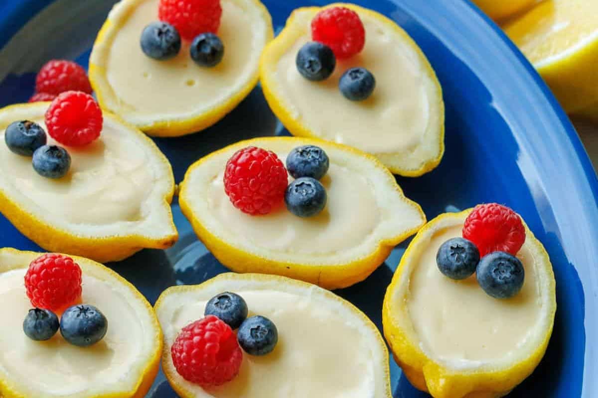 Halved lemons filled with creamy custard, topped with blueberries and raspberries, arranged on a blue plate—one of the prettiest desserts and a perfect addition to your spring desserts collection.