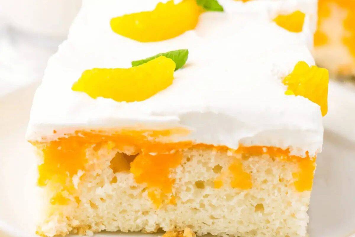 A slice of white cake topped with whipped cream, peach slices, and a small mint leaf, with visible peach pieces inside the cake—one of the prettiest desserts and perfect for spring recipes.