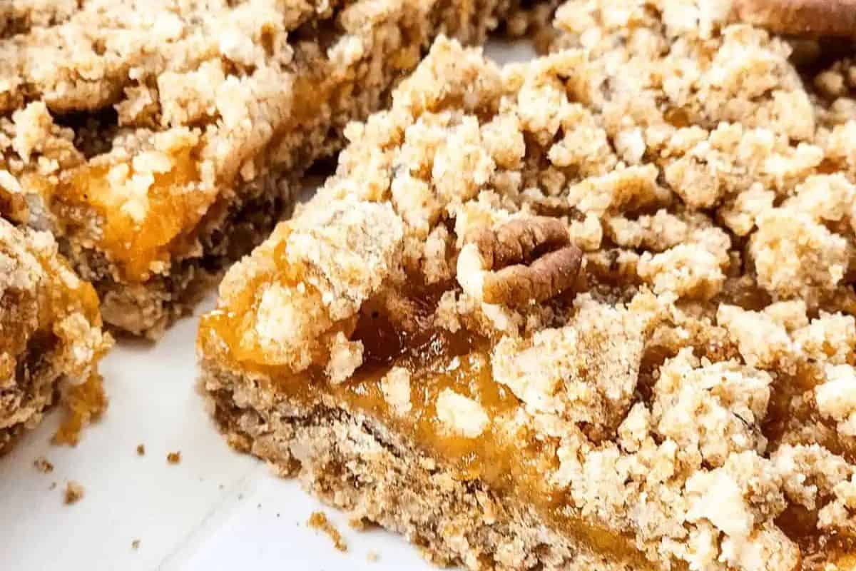 Close-up of crumbly dessert bars with a golden brown oat topping and a layer of orange filling, perfect for spring desserts or adding to your collection of the prettiest desserts on a white surface.
