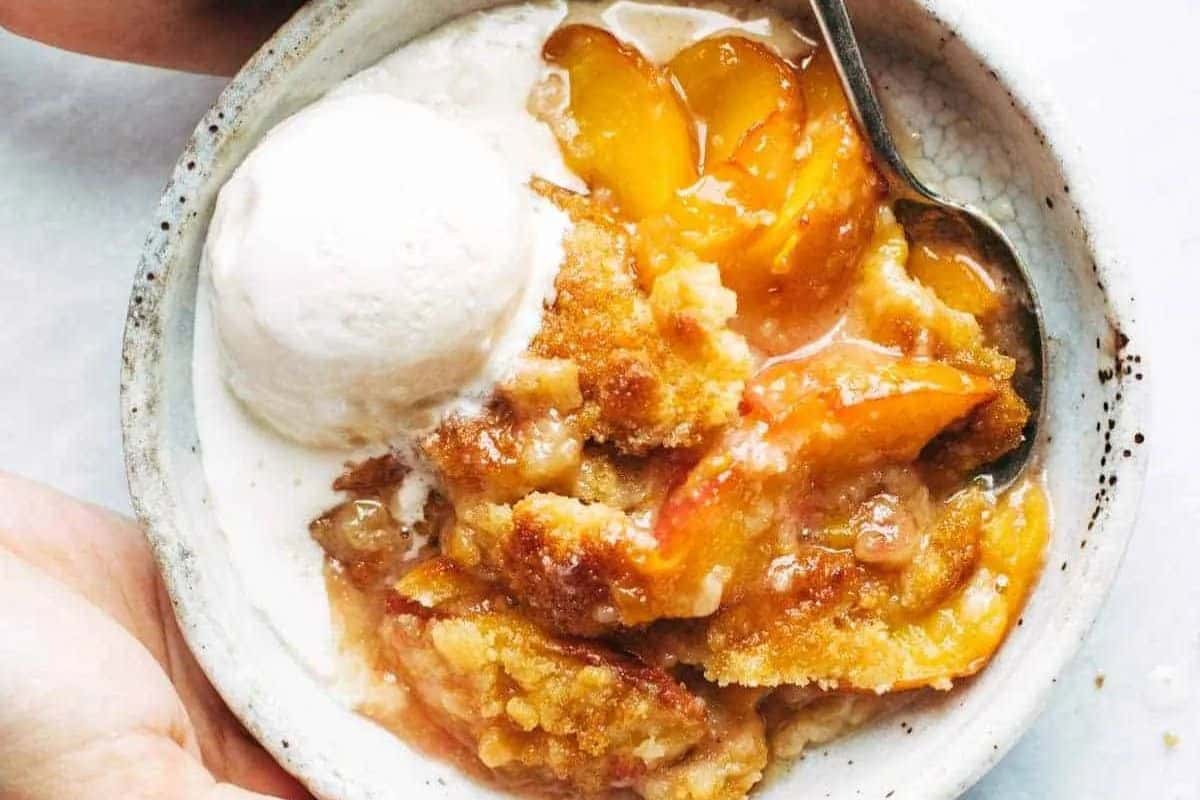 A bowl of peach cobbler with a scoop of vanilla ice cream and a spoon—one of the prettiest desserts and a classic choice for spring recipes.