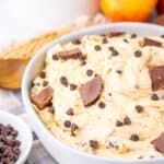 A white bowl filled with creamy dessert mixed with chocolate chips and topped with pieces of chocolate peanut butter cups.