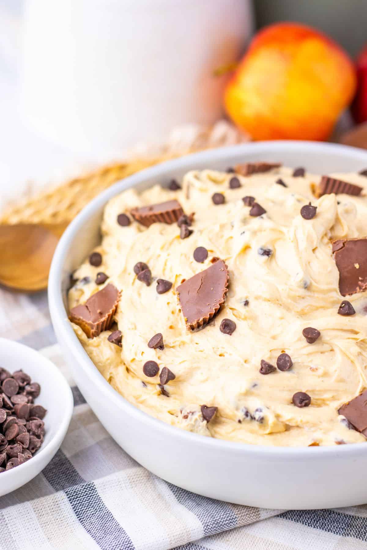 A white bowl filled with creamy dessert mixed with chocolate chips and topped with pieces of chocolate peanut butter cups.