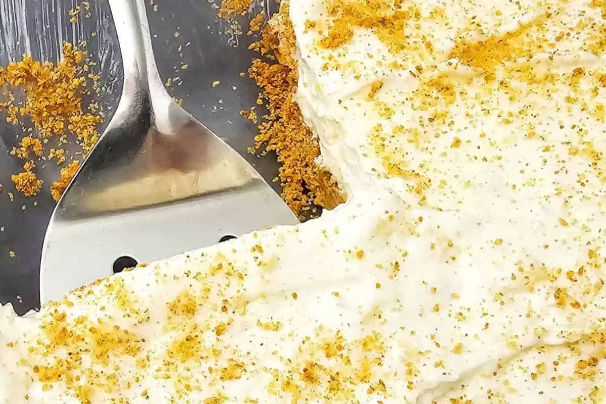 A metal spatula lifts a slice of creamy dessert with a graham cracker crumb crust and sprinkled crumbs on top—one of the prettiest desserts perfect for spring recipes.